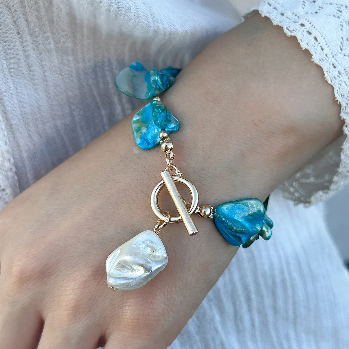 Bracelet bohème chic avec breloques en nacre bleue et blanche, fermoir doré, parfait pour un look estival.