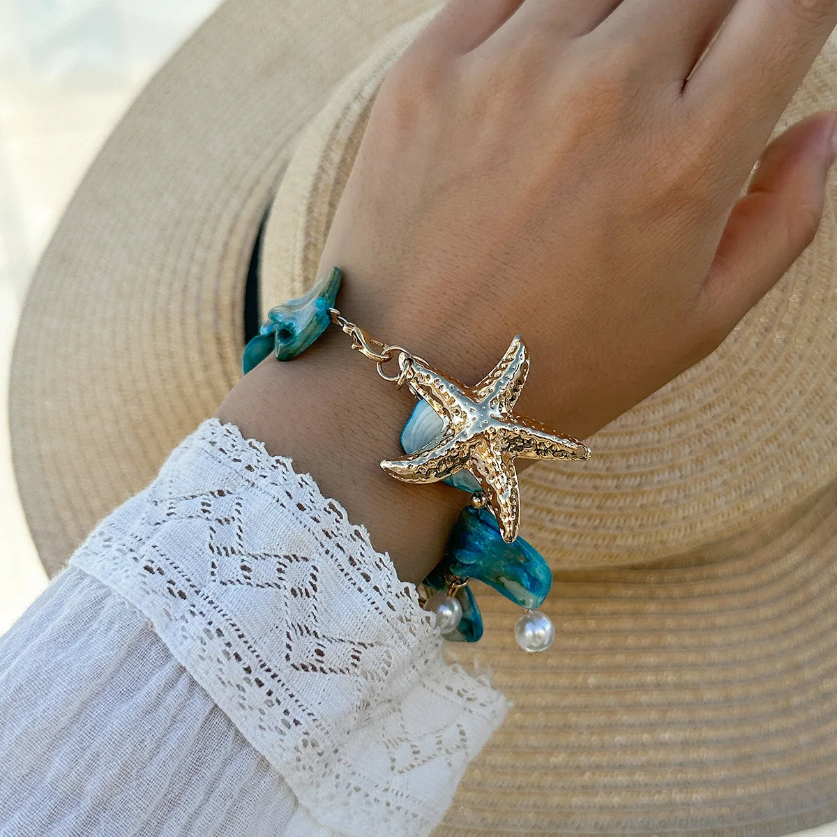Bracelet bohème chic avec breloques étoile de mer, nacre et perles, sur une main portant un vêtement blanc en dentelle.