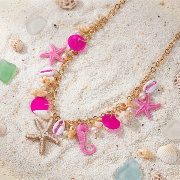 Collier doré festif avec breloques étoiles de mer, hippocampes, coquillages et perles, ambiance plage tropicale.